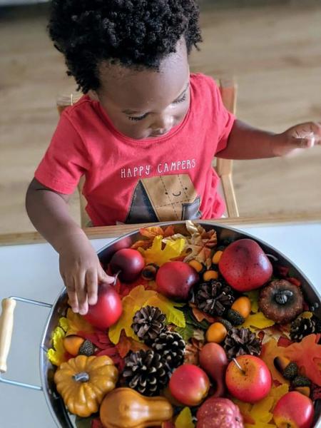 child touching bowl filled with apples, pumpkins, leaves and pinecones